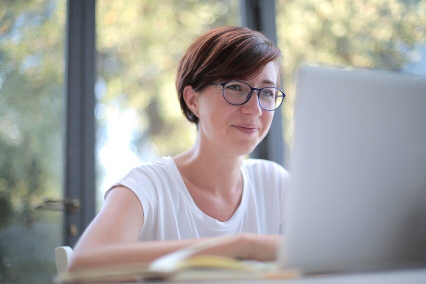 A woman wearing glasses is sitting at a table with a laptop, focusing on her MCCQE1 exam preparation.