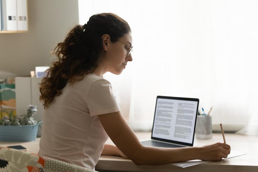 A woman working on her laptop at home, preparing for the MCCQE1 exam.