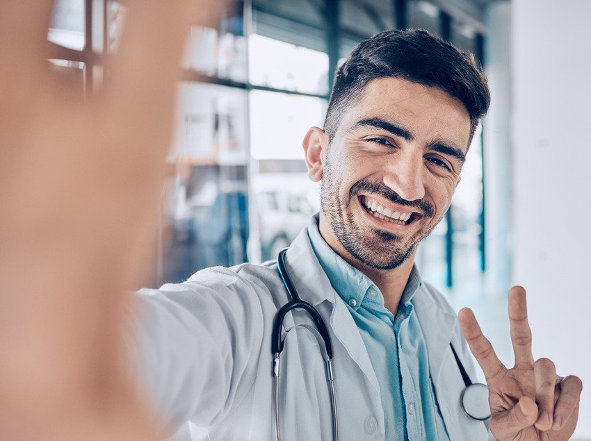 A male doctor confidently making a peace sign while studying for the MCCQE1 exam using Ace QBank.