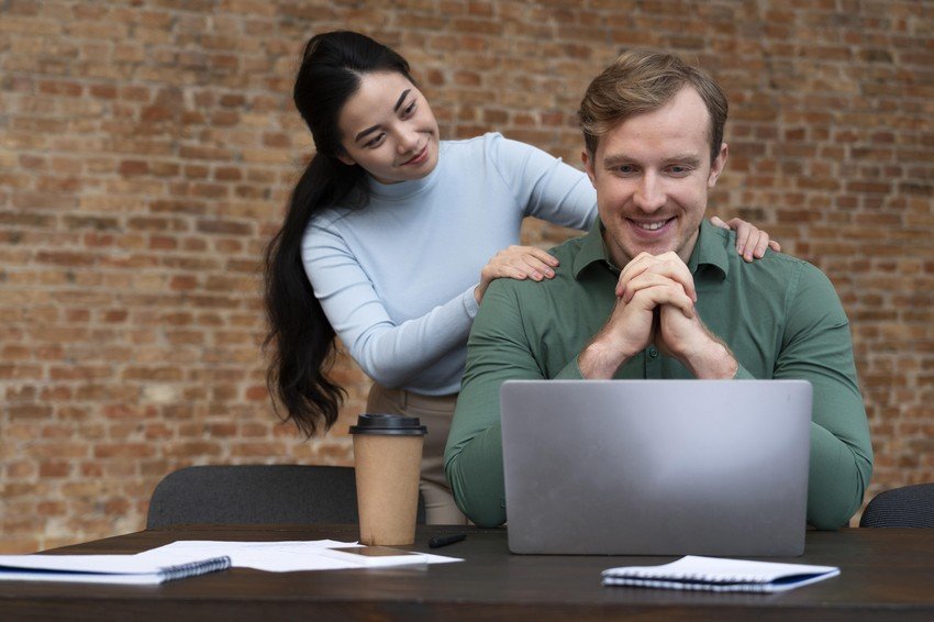 A man and woman sitting at a desk with a laptop, looking at the MCCQE1 self-assessment result.