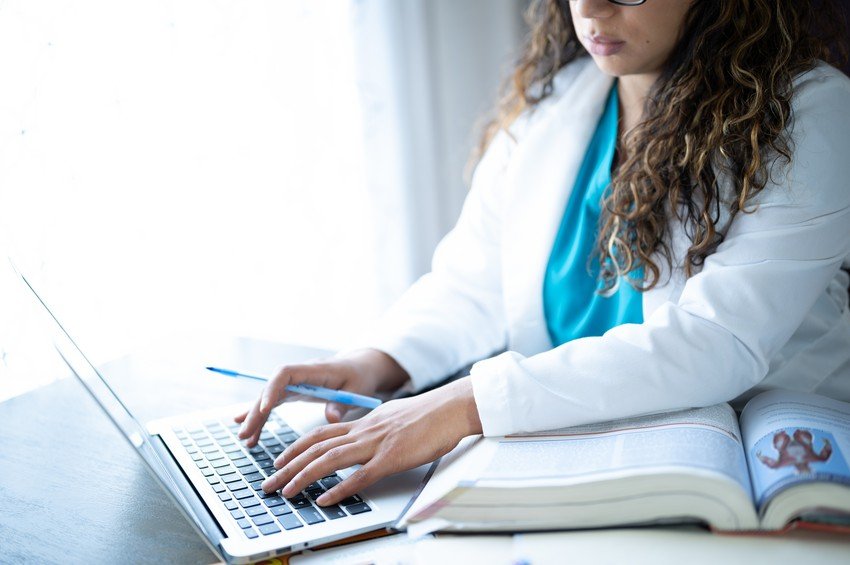 A doctor preparing for the MCCQE1 exam is working on a laptop at a desk.