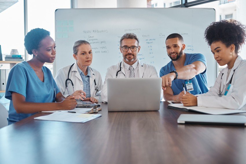 A group of doctors, familiar with the MCCQE Part 1 exam, sitting around a table looking at a laptop.