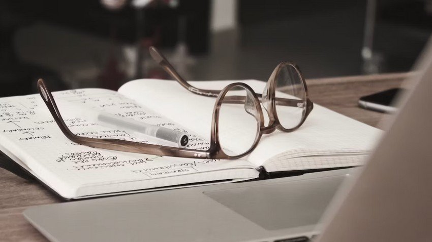 On a desk, you will find a notebook and glasses alongside a laptop with the Ace QBank website open.