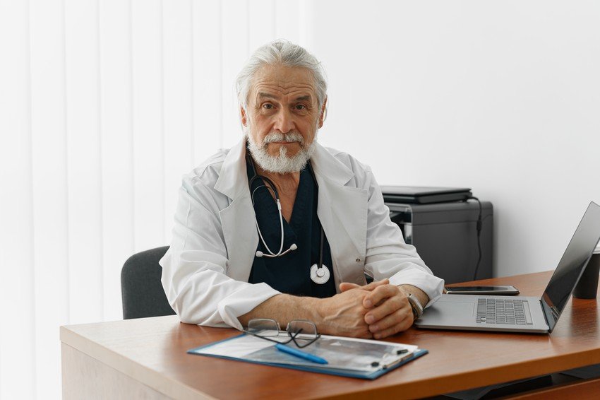 A doctor sitting at his desk with a laptop, studying for the MCCQE Part 1 using a question bank.
