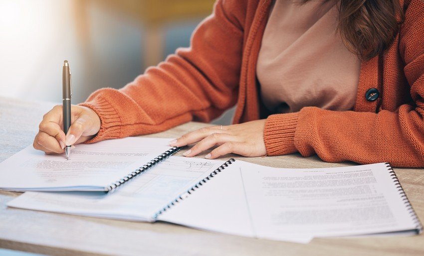 A woman prepares for her MCCQE1 exam, writing in a notebook with a pen while utilizing the helpful Ace QBank for last-minute review.