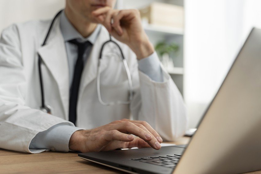 A medical student in a white coat is using a laptop for MCCQE1 exam preparation.