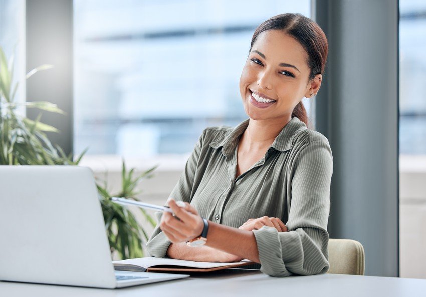 Professional woman smiling at the camera while holding a pen, with a laptop displaying Ace QBank for MCCQE1 exam preparation in front of her.