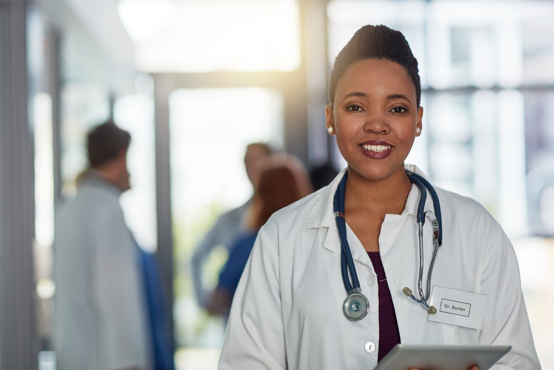 A smiling doctor holding a tablet in a busy hospital ward, using Ace QBank for MCCQE part 1 prep.