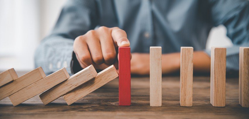 A person's hand stops a row of falling dominoes to avert a chain reaction, highlighting the red domino as a sign of managing stress during MCCQE1 exam preparation.
