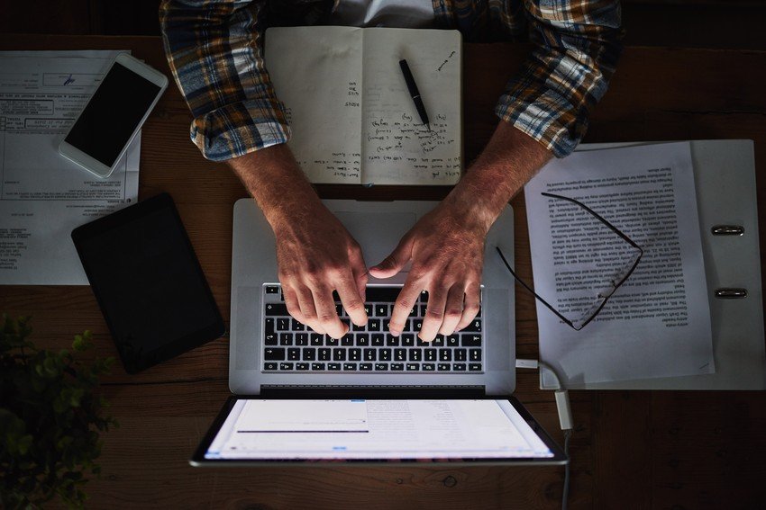 Person working on a laptop surrounded by documents, an Ace QBank for MCCQE1 study plan, and a smartphone.