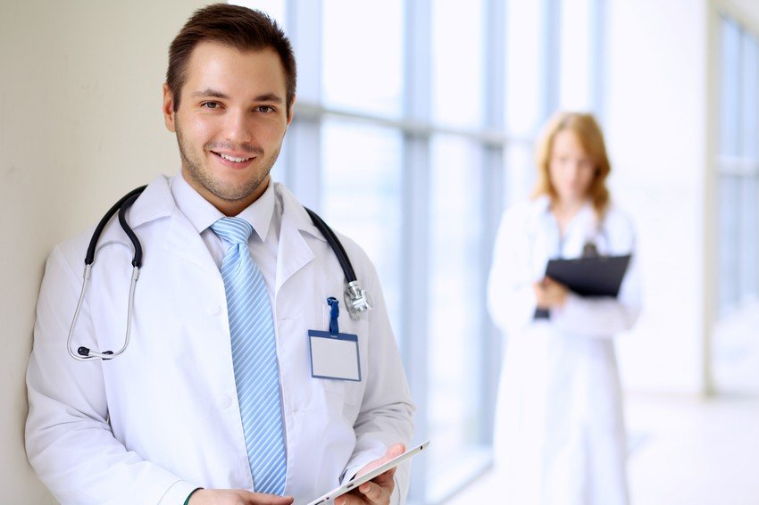 A male doctor with a stethoscope is smiling at the camera, and a female colleague discussing MCCQE Part 1 Prep Hidden Costs & Risks.