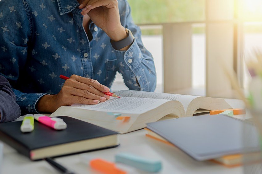 Person studying with highlighters and books on a table, marking text while deep in thought for MCCQE1 exam preparation.