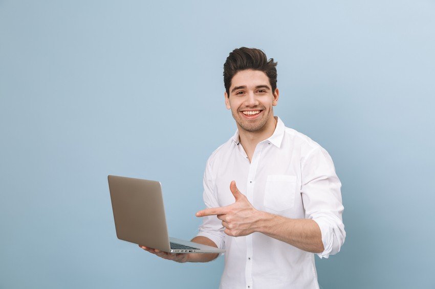 Man in a white shirt smiling, holding and pointing at an open laptop displaying Ace QBank online question bank for MCCQE1 against a light blue background.
