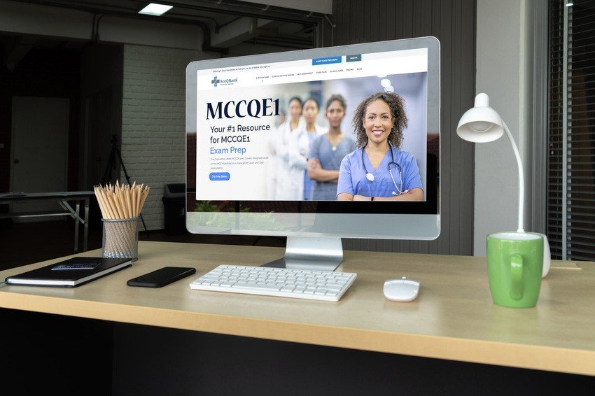 A desktop computer on a wooden desk displays the Ace QBank website for MCCQE1 exam prep. Pencils, a smartphone, keyboard, and a green mug are also on the desk.
