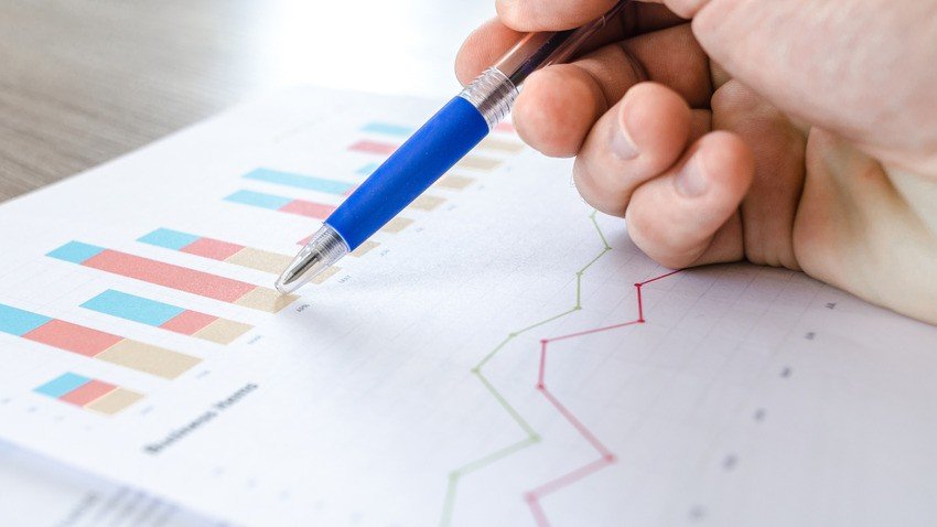 A hand holding a pen points to a printed page with colorful bar and line charts, illustrating data for MCCQE1 self-assessment —perfect for Ace QBank users focused on MCCQE Part 1 Prep.