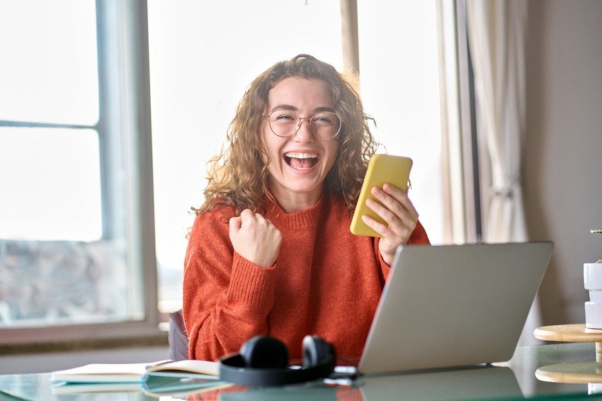 A woman with curly hair and glasses is seated at her desk with a laptop open to Ace QBank materials, headphones nearby, diligently preparing for the MCCQE Part 1 by the window.