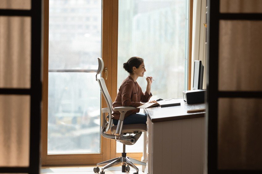 A person sits at a desk in a home office, focused intently on their computer screen. Large windows provide natural light in the background as they review Ace QBank questions to ace the MCCQE Part 1 exam.