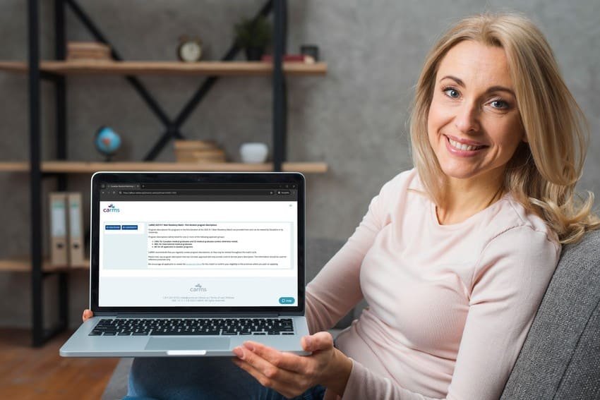 A woman sitting on a couch smiles and holds a laptop displaying the Ace QBank website, known for its MCCQE1 exam prep resources and user-friendly interface with helpful text and buttons.
