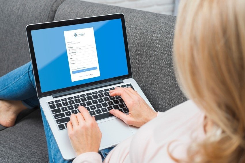 A person sits on a couch using a laptop displaying an Ace QBank sign-up form for MCCQE1 exam preparation.