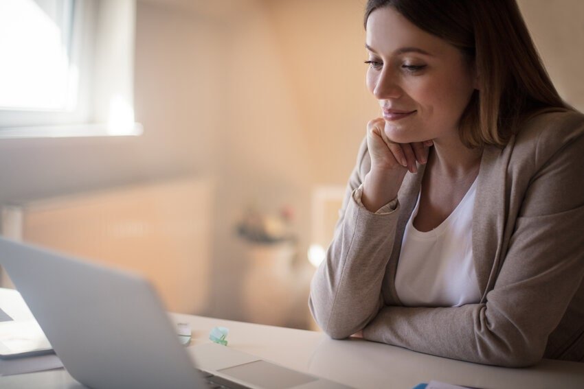 A woman studying on a laptop in a well-lit room, focused and smiling slightly, representing preparation for the MCCQE1 exam using Ace QBank, an IMG-friendly resource for MCCQE1 exam prep.