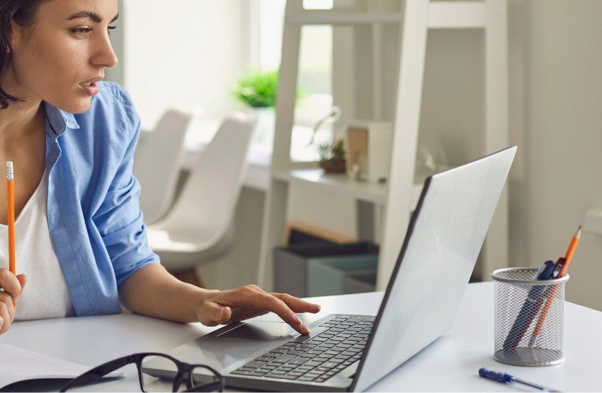 A person sits at a white desk, using a laptop with one hand and holding a pencil with the other. Perhaps exploring how to use Ace QBank effectively for MCCQE1. A pen holder and eyeglasses are also on the desk.