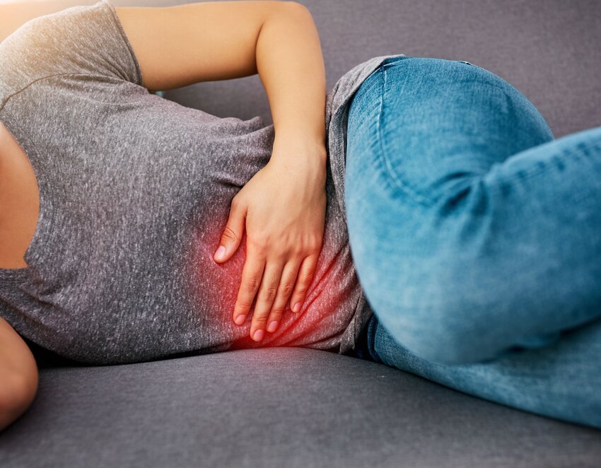 A person lying on a couch, clutching their lower abdomen in pain, with a red glow highlighting the area. Representing a clinical edge in Ace QBank.